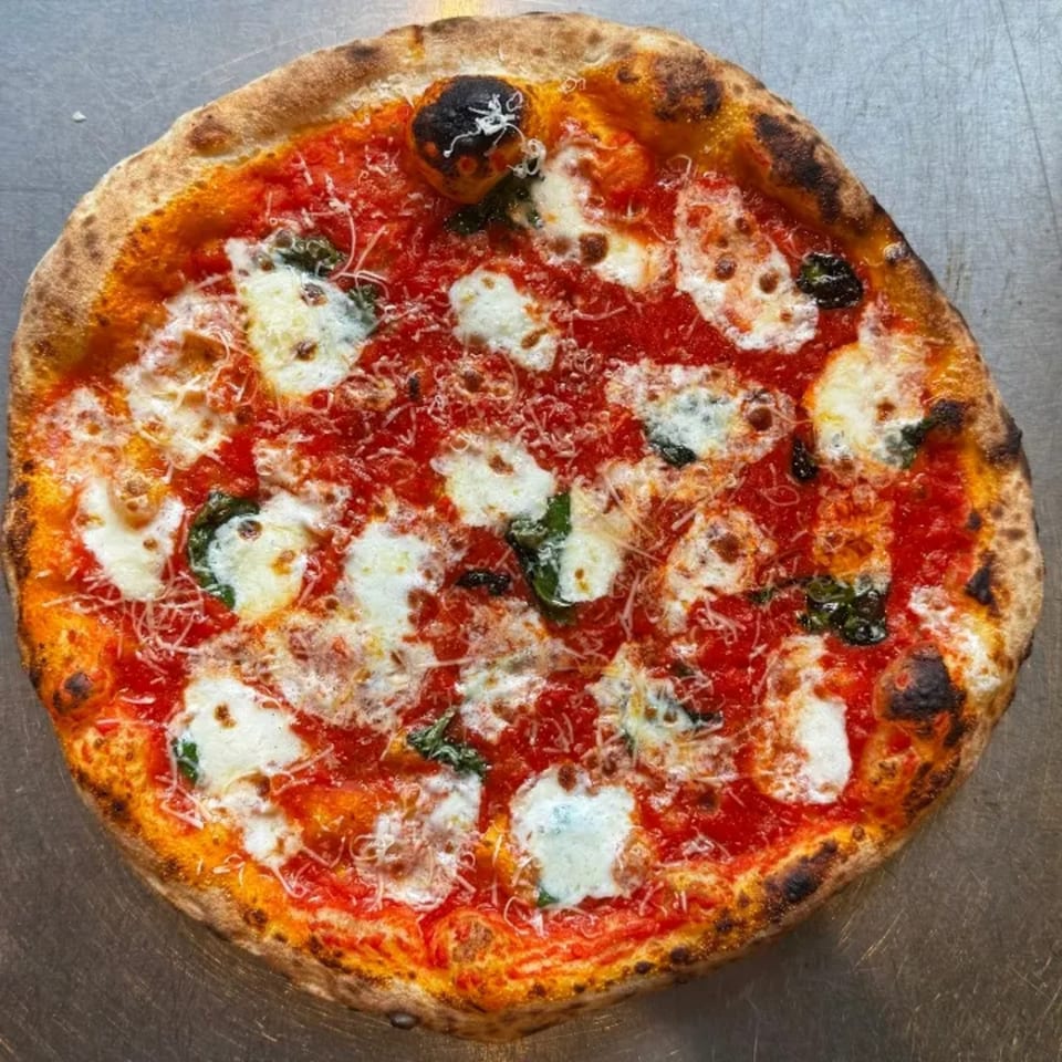 A freshly baked Neapolitan pizza with bright red sauce, melted mozzarella, and basil on a metal surface.