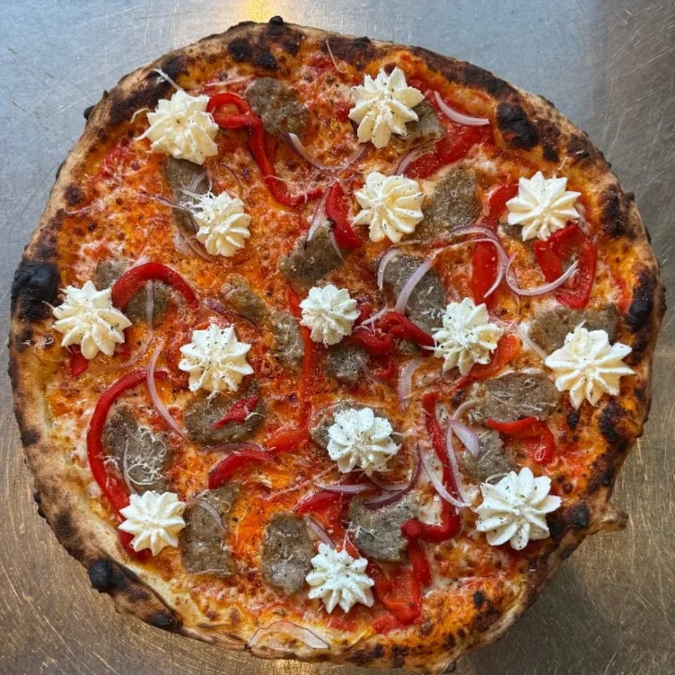 A whole pizza with red peppers, sausage, red onions, and dollops of white cheese.