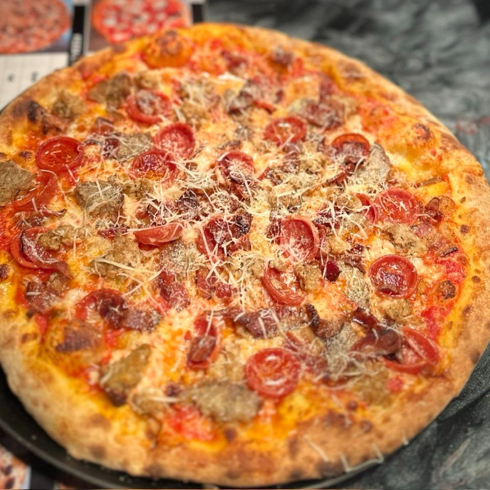 A whole pizza with pepperoni, sausage, and shredded cheese on a dark surface.